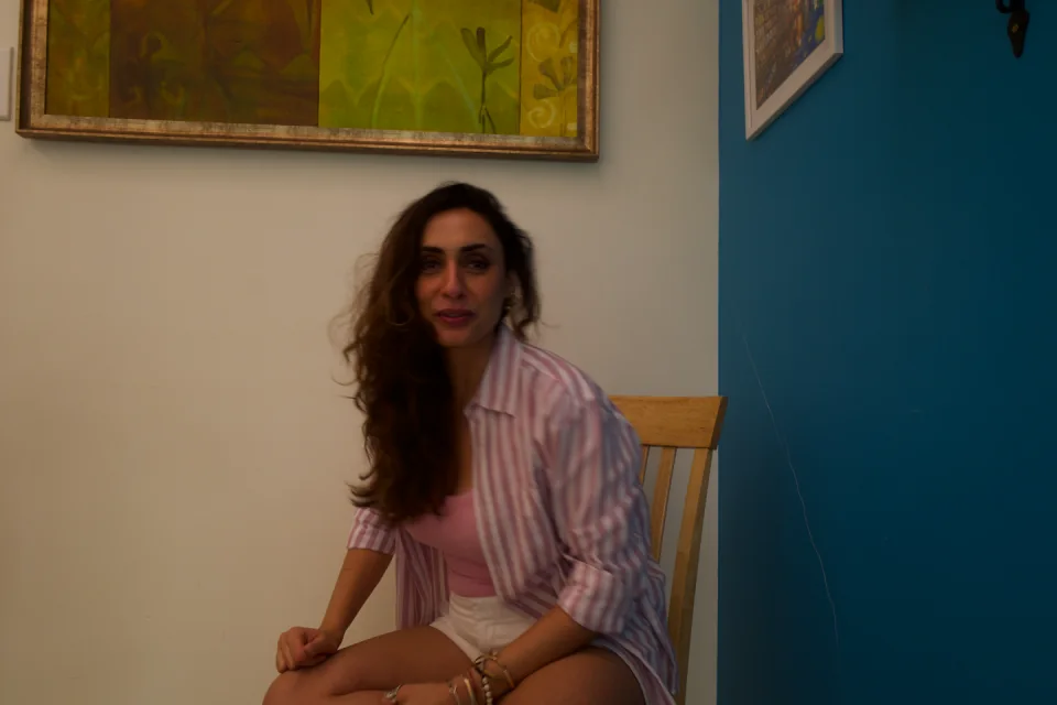 Sabah seated in a striped shirt beside a blue wall